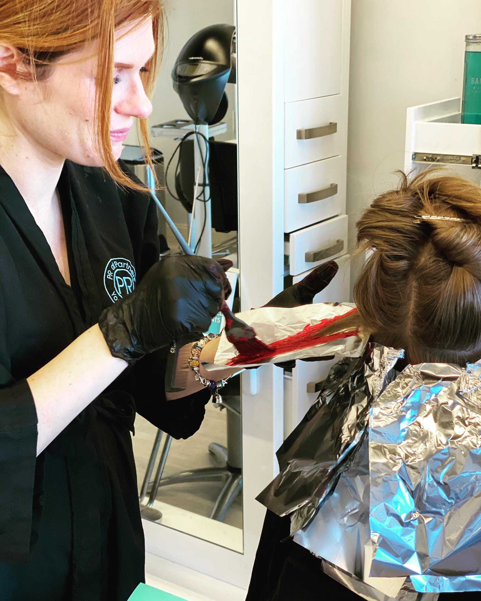 Hair stylist applying color to client's hair with brush and foil in salon.